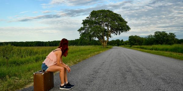 A woman in denim shorts and pink top sits on luggage waiting by the road in Estonia.
